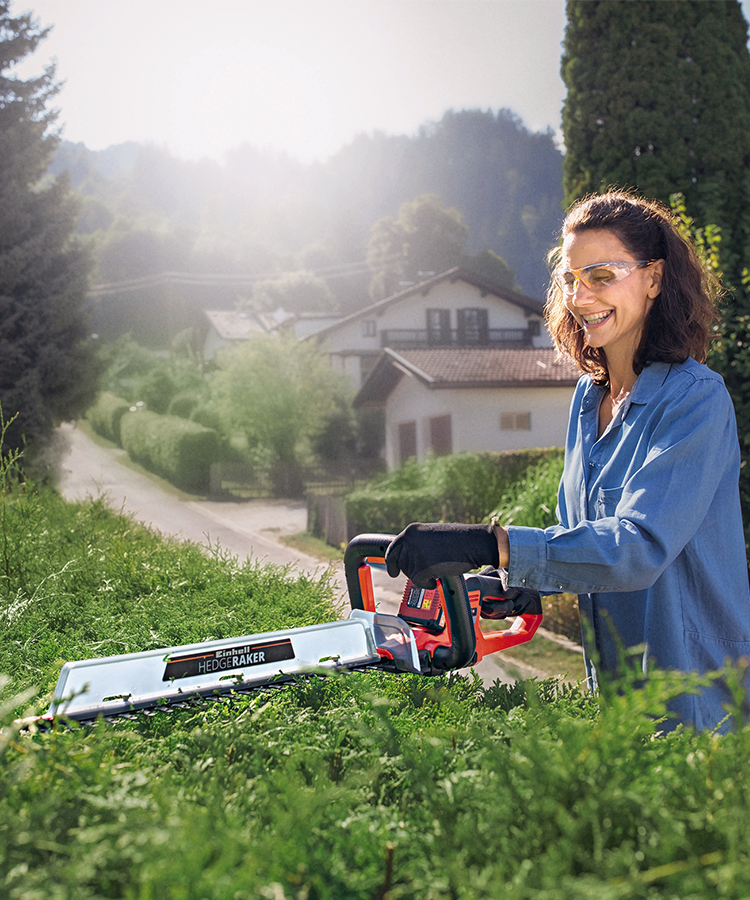 Woman with hedge trimmer cutting bush