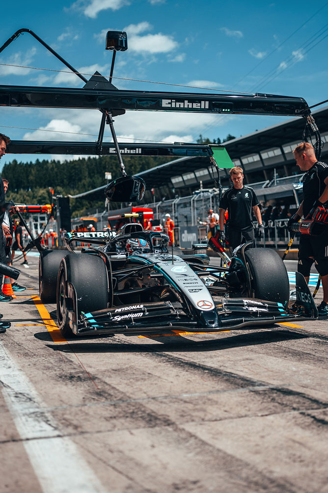 Um carro de Fórmula 1 Mercedes-AMG está nas boxes, rodeado por membros da equipa sob uma estrutura de garagem Einhell.