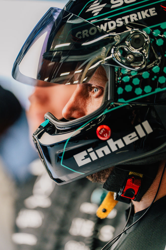 Um membro da equipa de Fórmula 1 está a usar um capacete e a olhar para o lado com atenção.